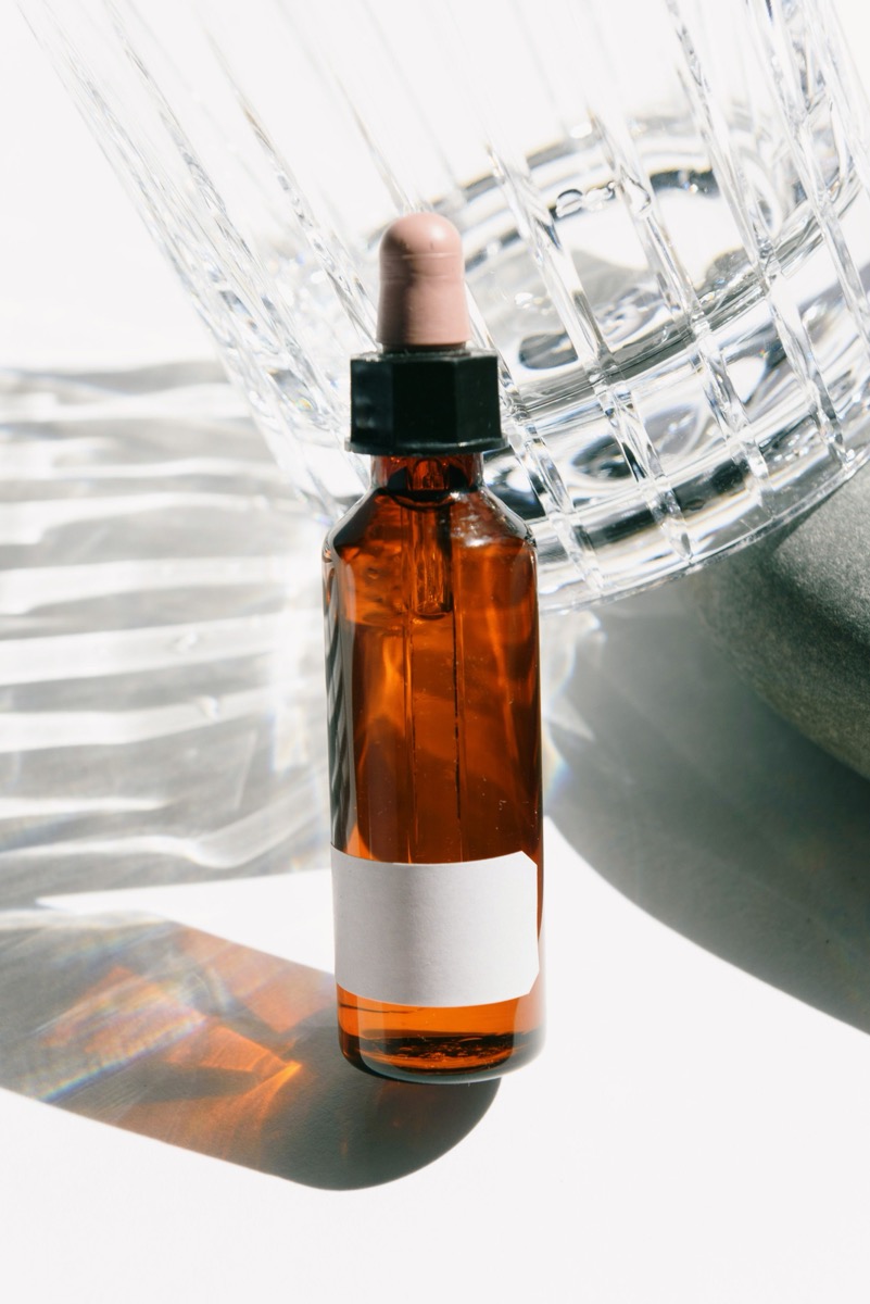 Original photo of an amber dropper bottle beside clear glass in direct sunlight